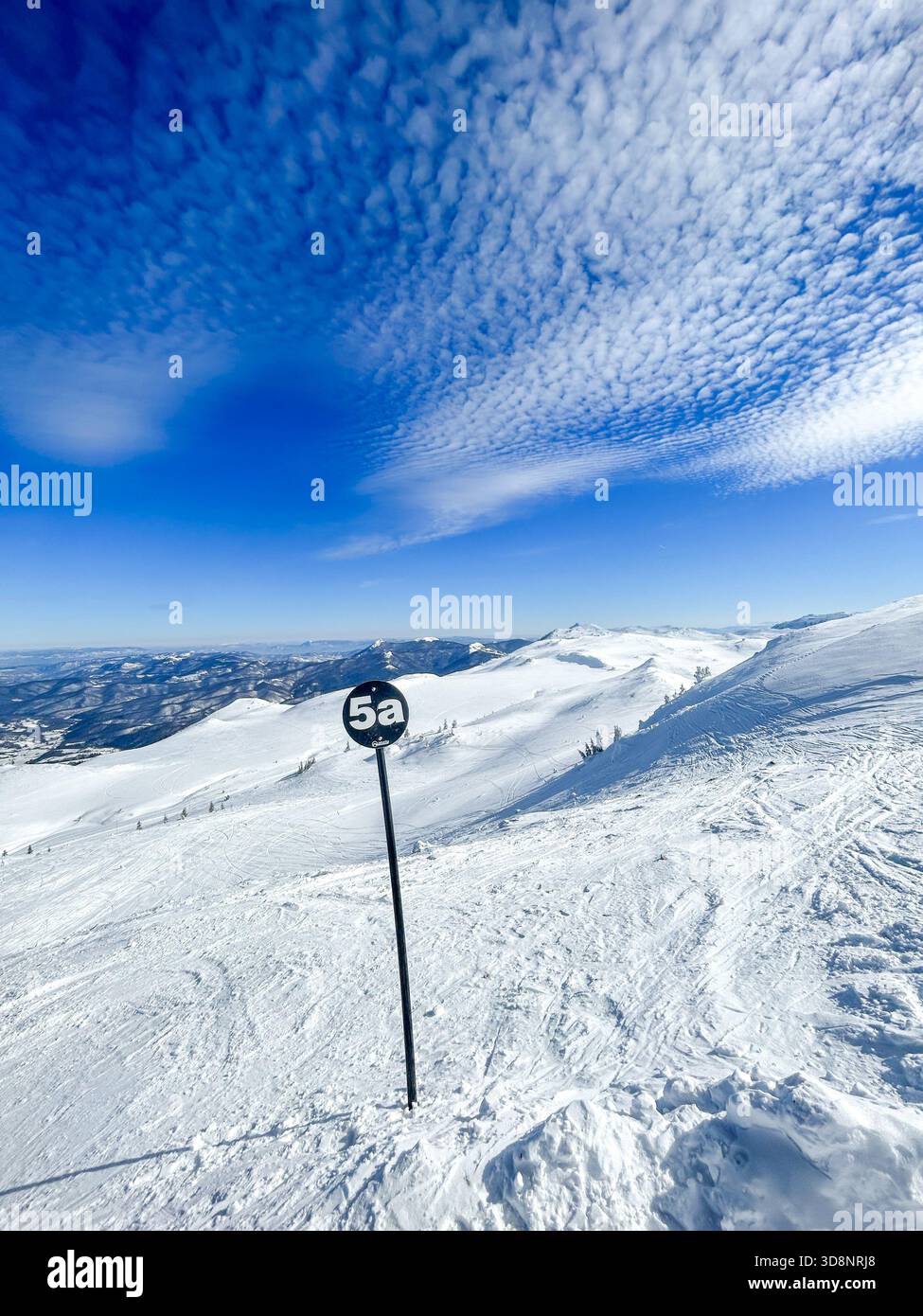 Vista sulla vetta innevata di Jahorina, caratterizzata dalla pista nera marcata 5a sotto spettacolari motivi nuvolosi e dalla luce invernale brillante. - Immagine stock catturata con smartphone