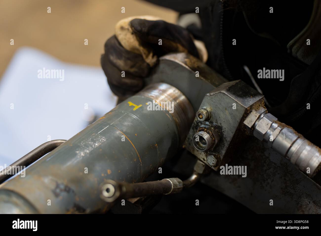 Tecnico meccanico che utilizza i guanti per la manutenzione del collegamento del cilindro idraulico, concentrandosi sul giunto filettato, sui raccordi in metallo e sulla manutenzione industriale Foto Stock