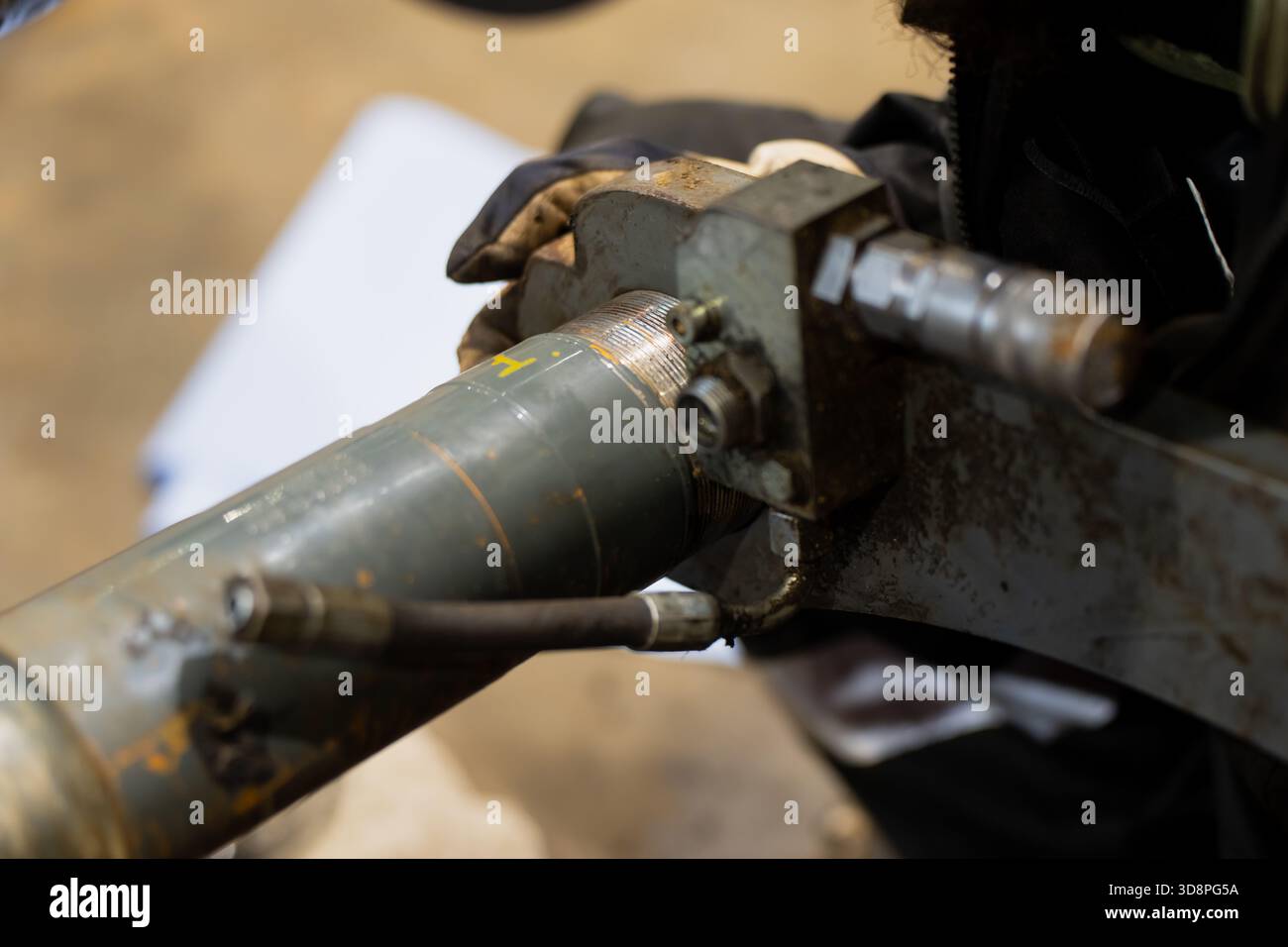 Meccanico che esegue la manutenzione del complessivo cilindro idraulico, afferrando la sezione metallica filettata e i raccordi con guanti protettivi durante la riparazione di precisione Foto Stock