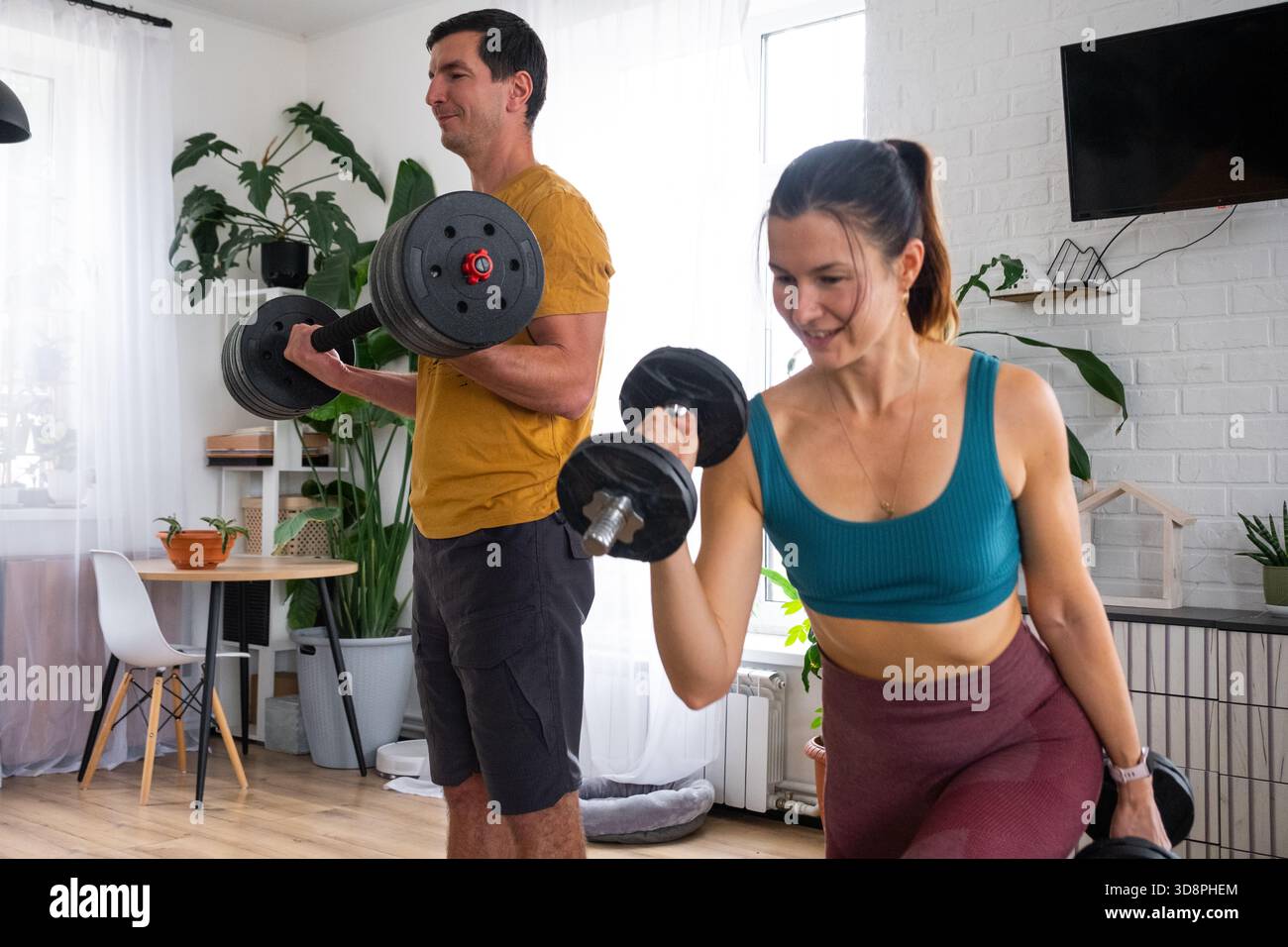 Donna e uomo in uniforme sportiva sono impegnati in fitness e allenamento di forza con un campanello e manubri a casa negli interni e nel gatto Foto Stock