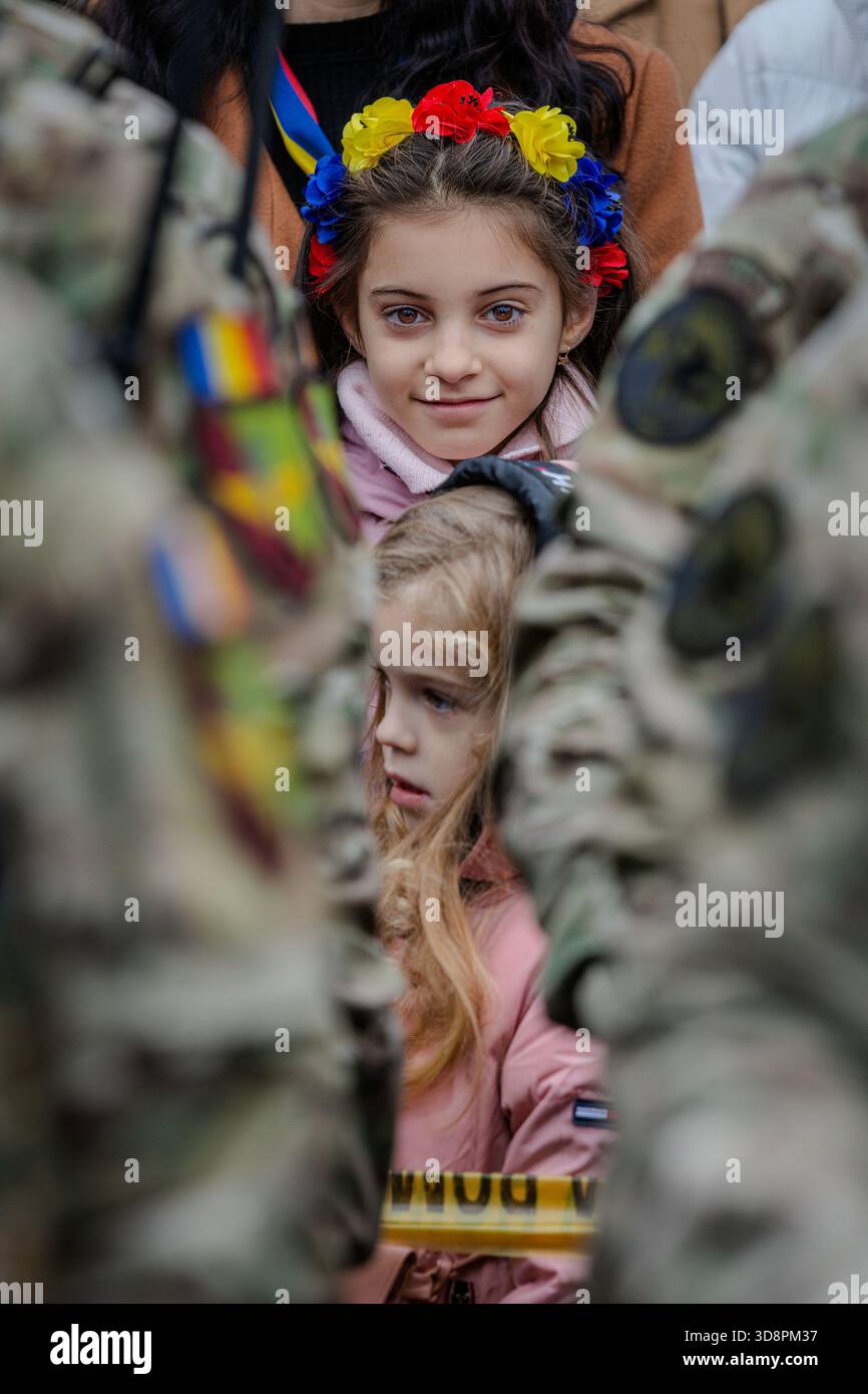 Bacau, Romania, 1 dicembre 2025: Due ragazze si sono schierate tra i soldati durante la giornata nazionale rumena a Piata Tricolorului, indossando un cerchietto tricolore in fiore Foto Stock