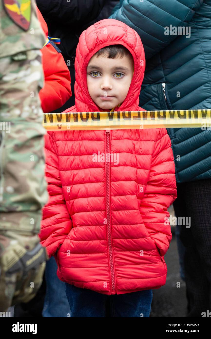 Bacau, Romania, 1 dicembre 2025: Un bambino in giacca rossa sta dietro il nastro di cautela durante le celebrazioni della giornata Nazionale a Piata Tricolorului. Foto Stock