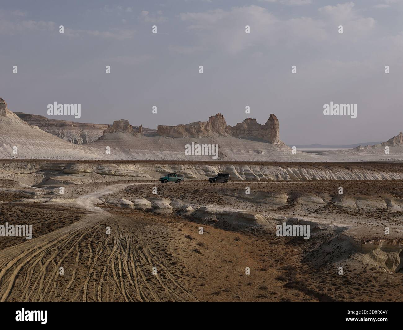 i suv fuoristrada attraversano una pista sterrata attraverso le scogliere bianche di gesso erose dell'altopiano dell'ustyurt e la vasta steppa arida, evocando avventure remote ed esplorazioni Foto Stock