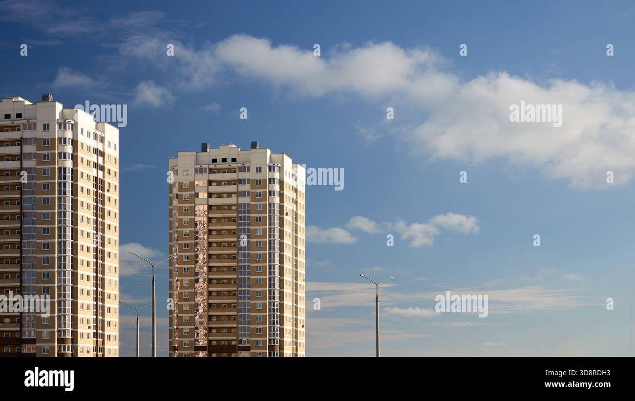 Architettura residenziale urbana con appartamenti a più piani e lampioni illuminati con il sole serale sotto il cielo blu con nuvole chiare e copia Foto Stock