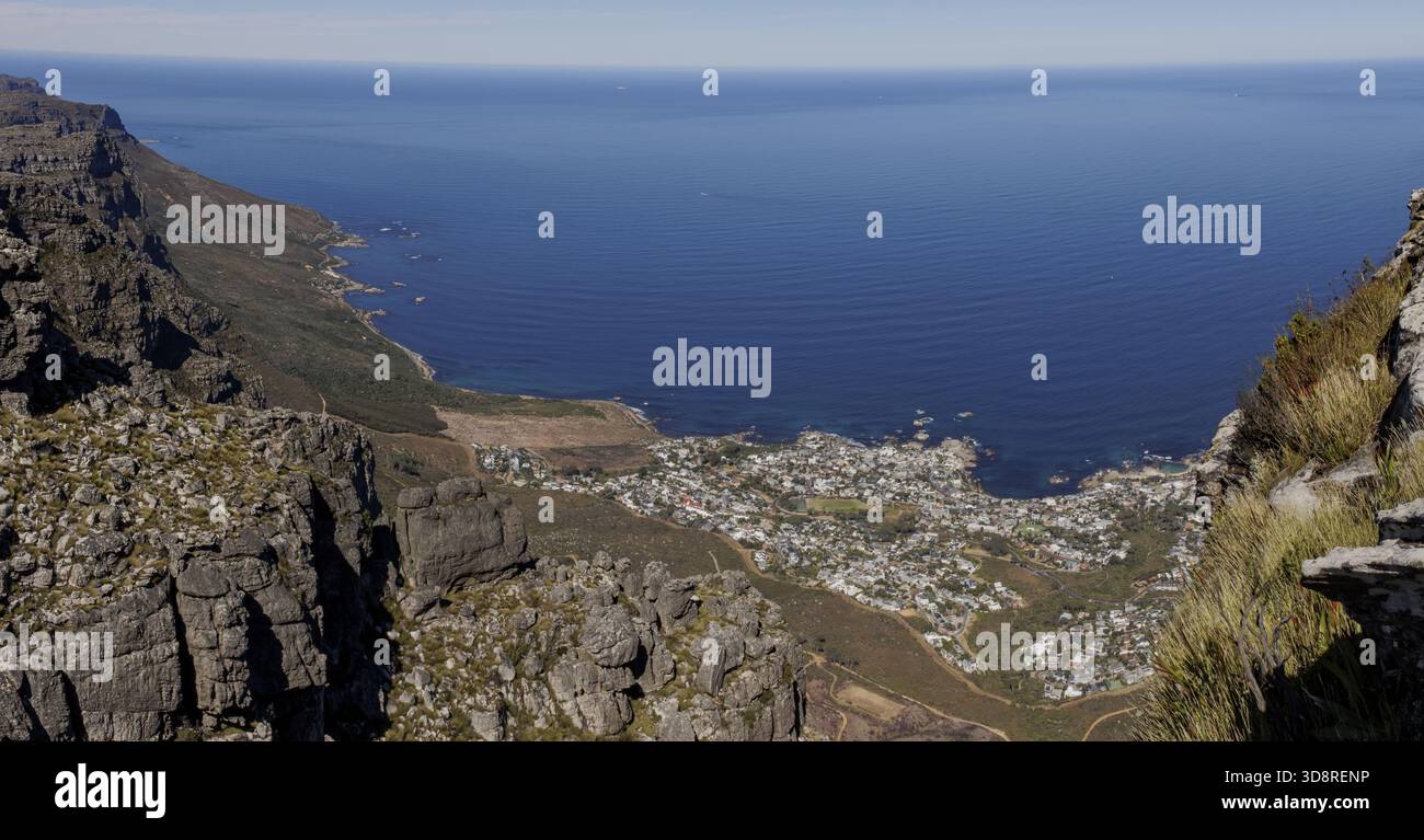 Vista aerea delle aspre montagne incontra il mare blu profondo, affacciato su una città costiera annidata sotto città del Capo, Capo Occidentale, Sud Africa. Foto Stock