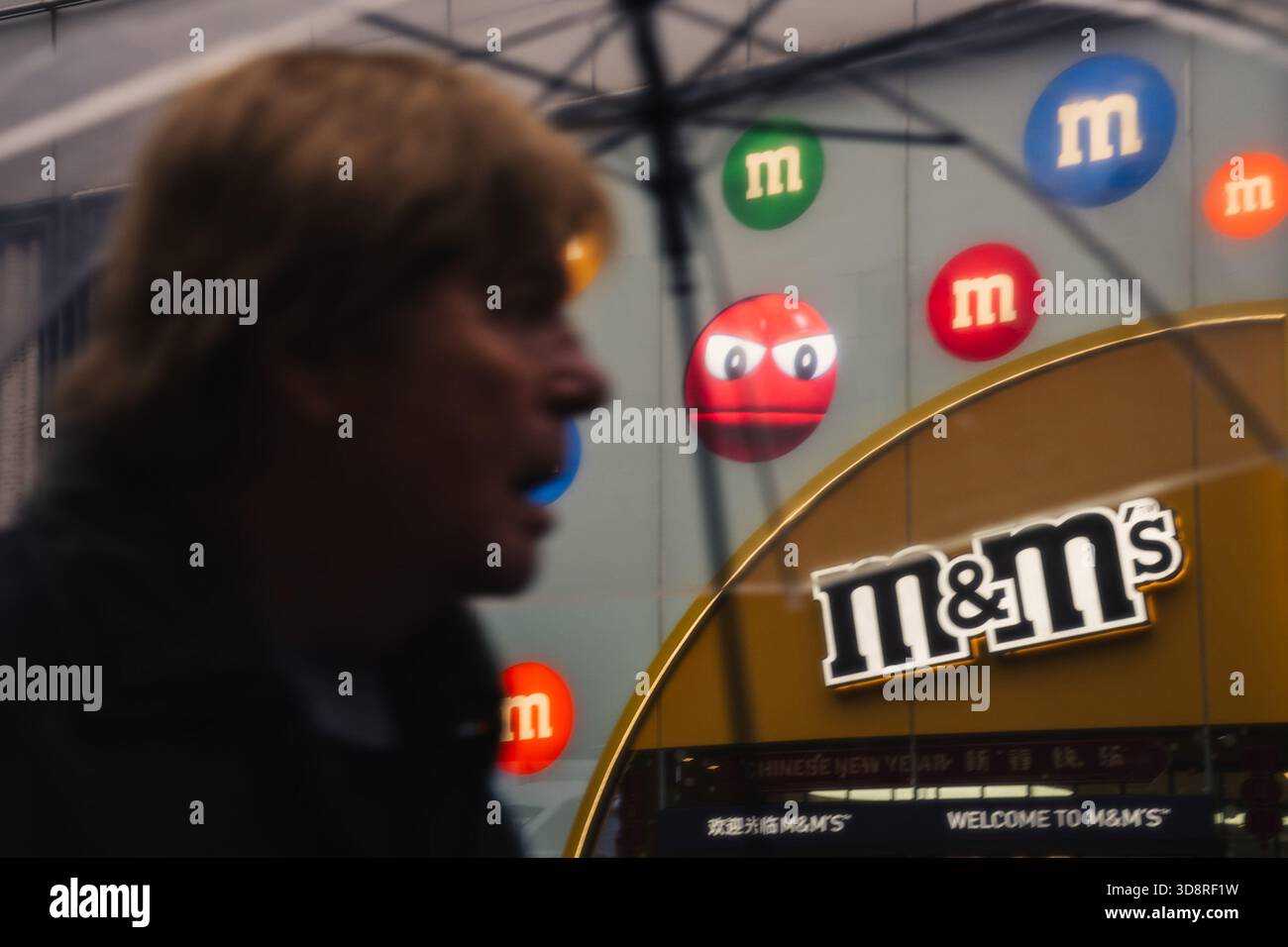 Shanghai, Cina - 25 novembre 2025: Vista di un pedonale che passa accanto al vivace negozio M&M's World, le sue iconiche caramelle colorate che spuntano contro il c Foto Stock