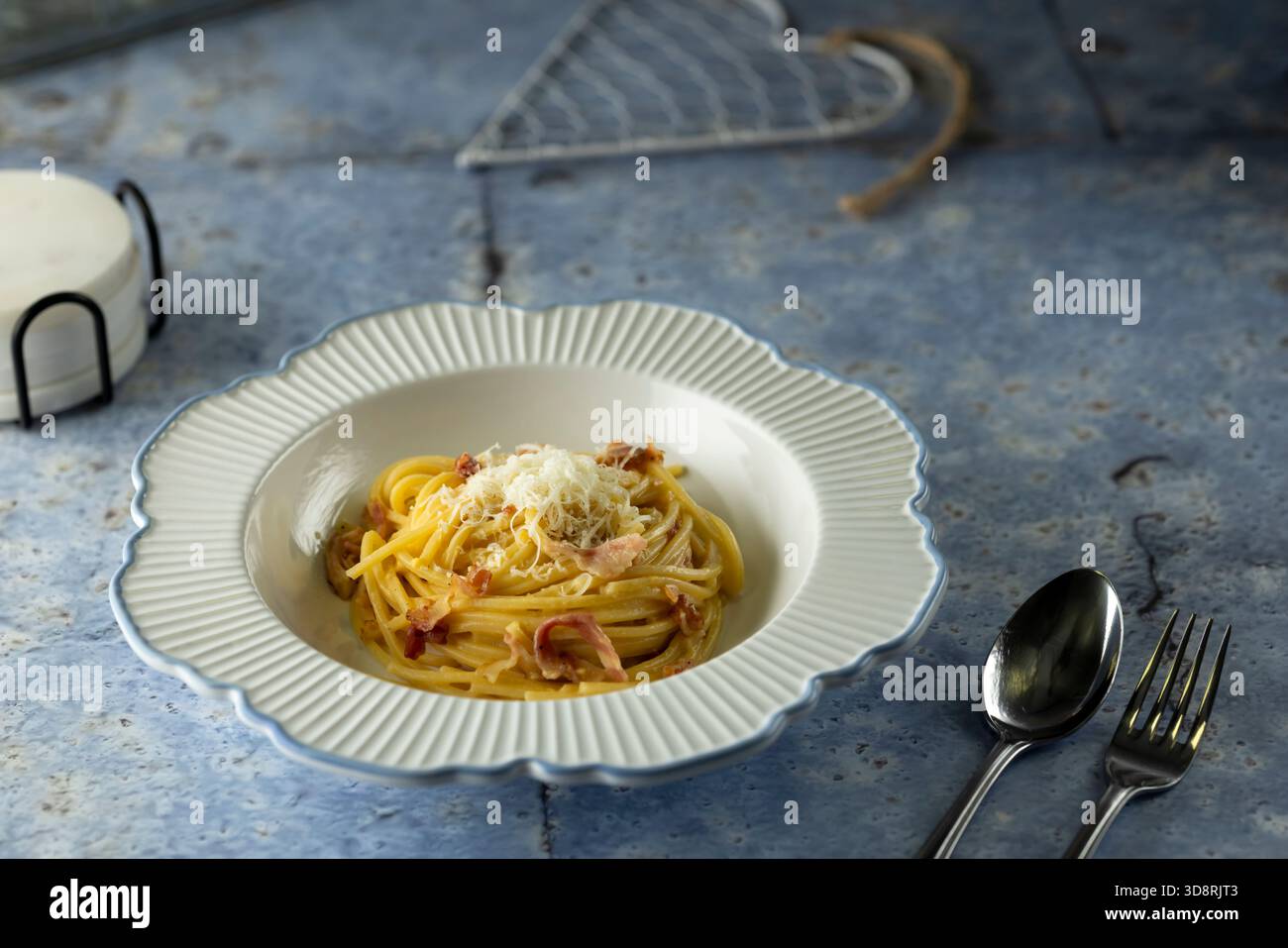 Cremosi spaghetti alla carbonara serviti in una ciotola bianca decorativa su sfondo blu Foto Stock