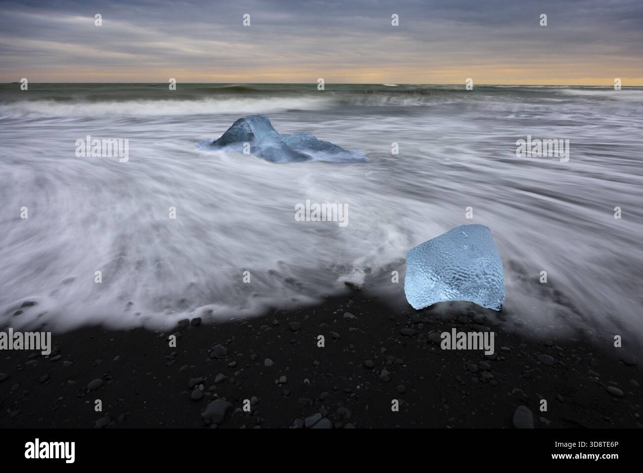 Vista del ghiaccio glaciale, blu scintillante contro la sabbia nera, baciato dall'abbraccio schiumoso delle onde dell'Atlantico sotto un cielo lunare, Diamond Beach, Sveit Foto Stock