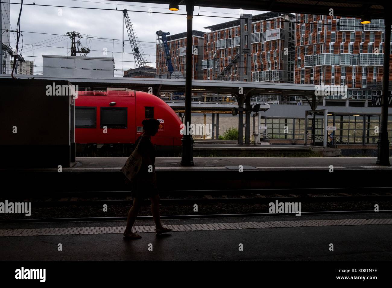 Persona che cammina sul binario della stazione ferroviaria di Tolosa-Matabiau con un treno rosso e edifici moderni sullo sfondo a Tolosa in alta Garonna Foto Stock