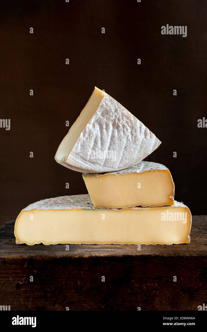 Tre pezzi di formaggio Saint-Nectaire sono impilati uno sull'altro, su una superficie di legno scuro, Puy de Dome, Auvergne, Francia Foto Stock