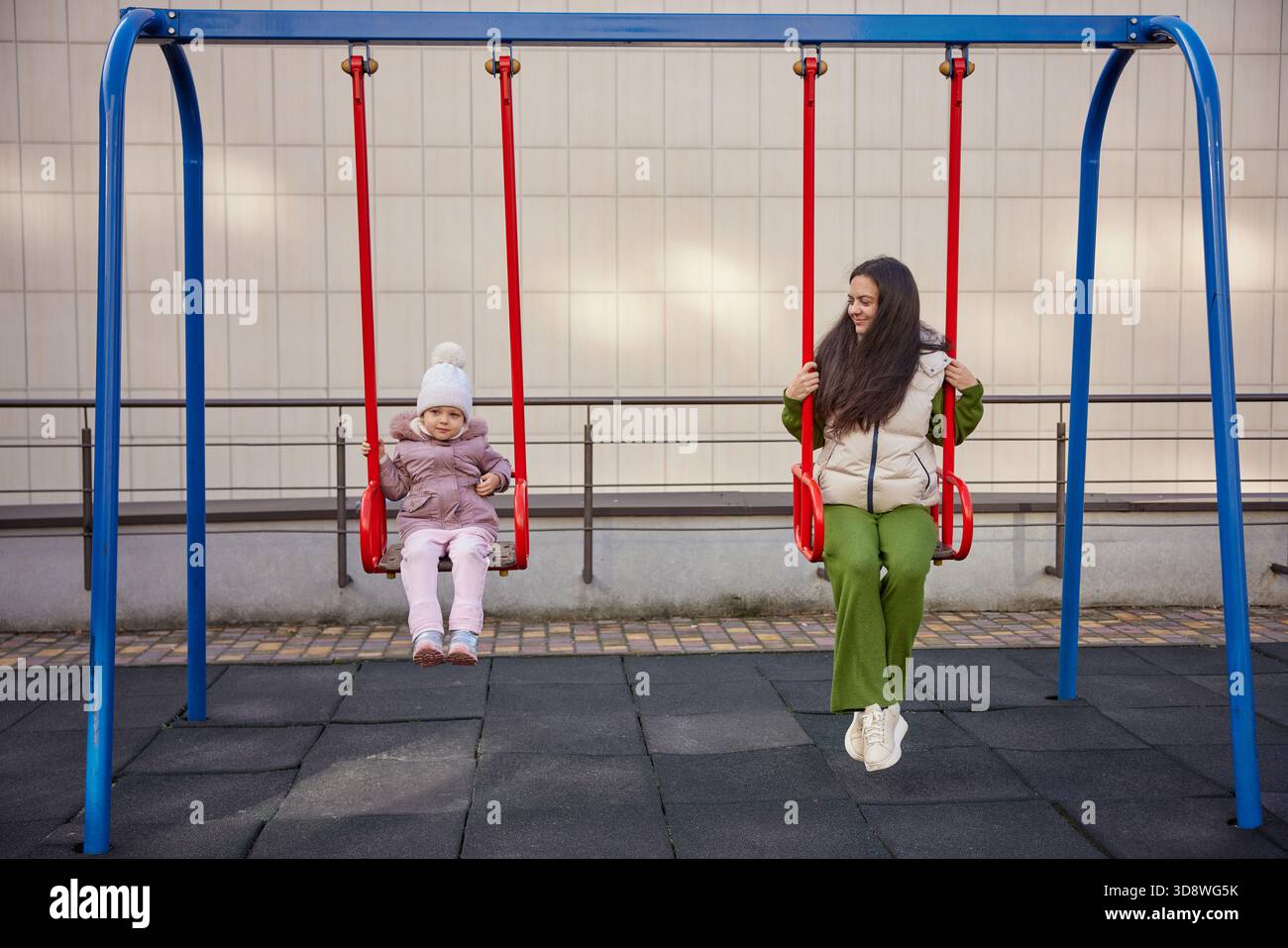 Madre e figlia dondolano, si divertono e si legano al parco giochi Foto Stock
