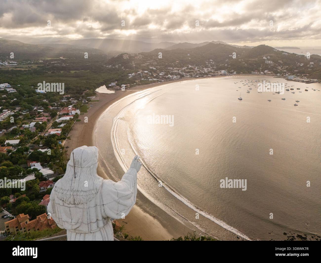 Una splendida vista sulla baia, affacciata su un tramonto, con una statua di rilievo. Le barche galleggiano pacificamente nell'acqua mentre il cielo si illumina. Foto Stock