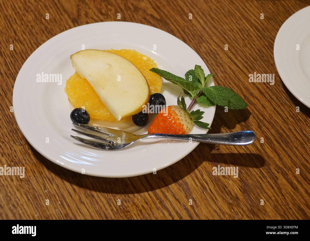 Piatto bianco con fette di vari frutti colorati decorato con foglie di menta; dessert, snack salutare, dessert vegeraziano. Foto Stock