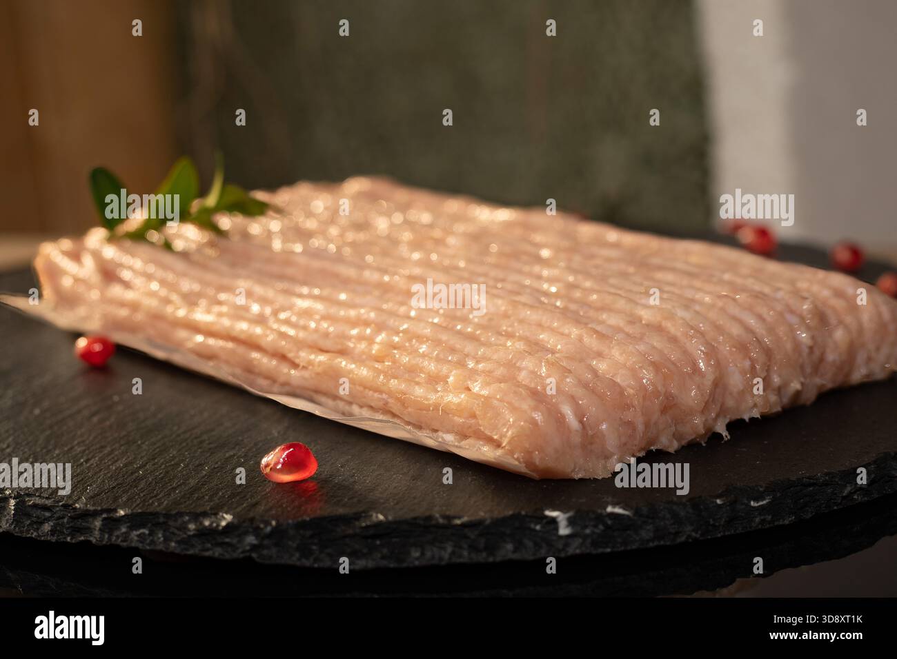 Filetto di carne macinata cruda fresca su piastra di pietra nera con erbe aromatiche e accenti di melograno Foto Stock
