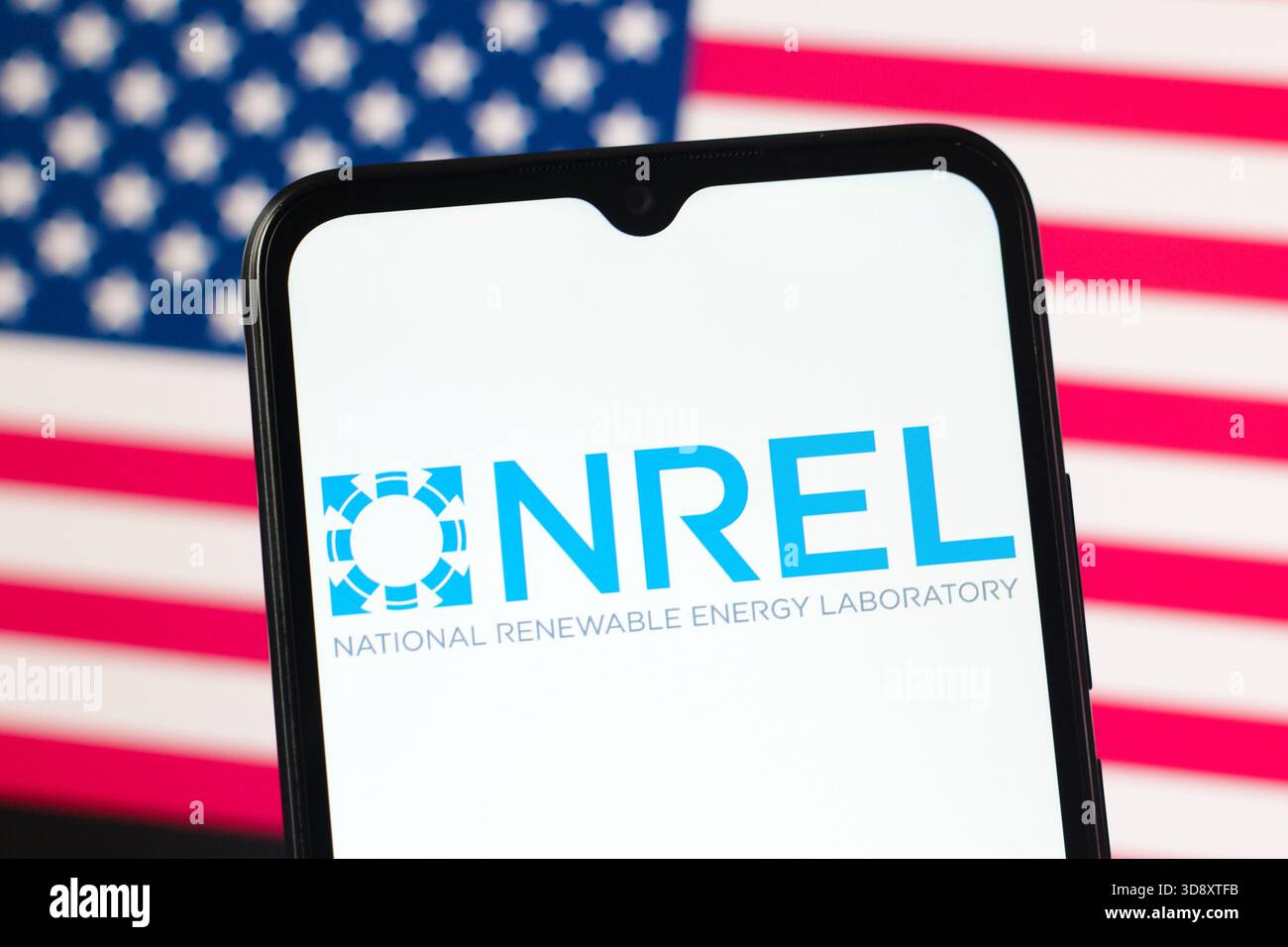In questa immagine, il logo NREL (National Renewable Energy Laboratory) è visualizzato sullo schermo di uno smartphone e la bandiera degli Stati Uniti sullo sfondo. Foto Stock