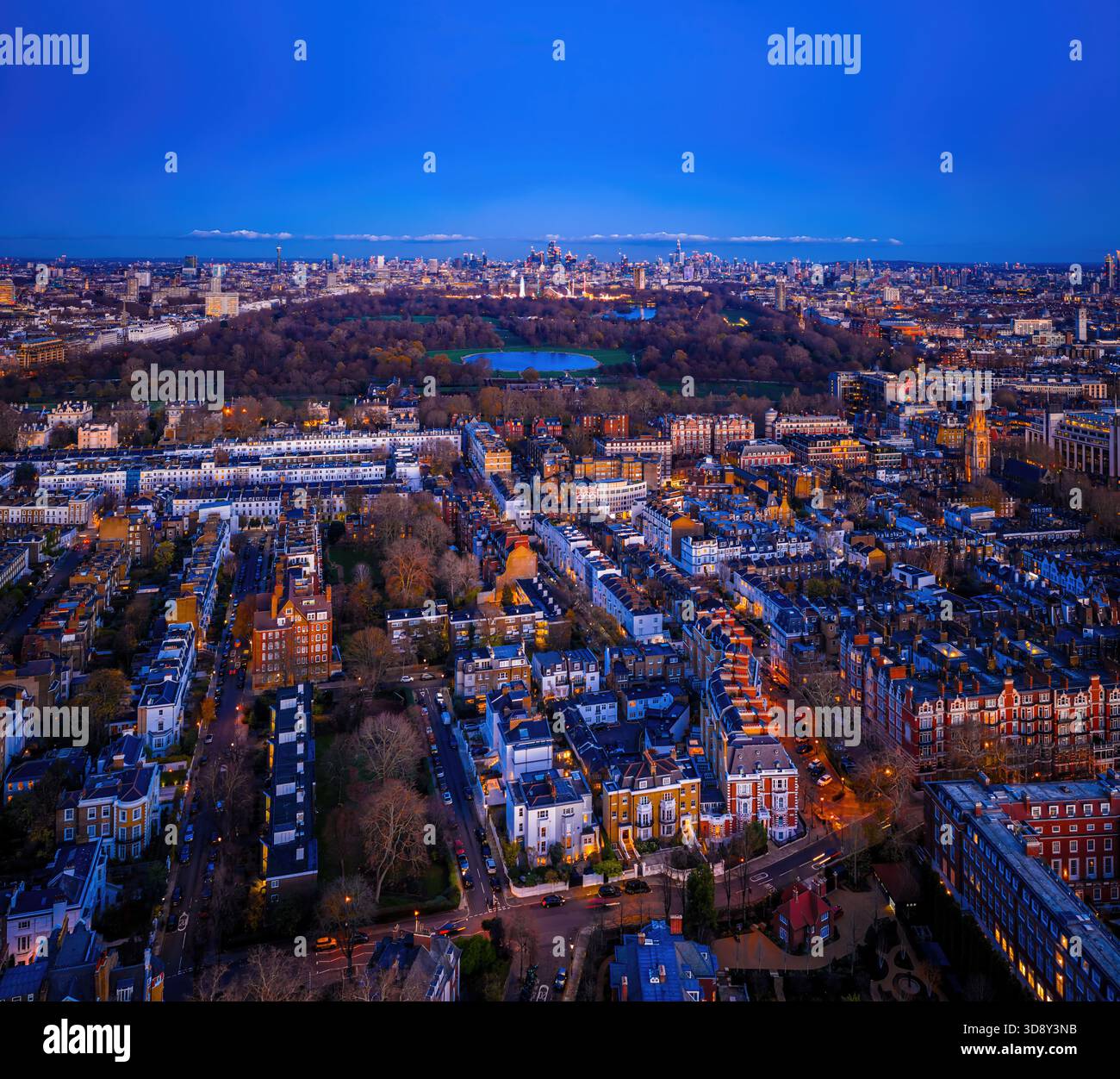 Splendida antenna al crepuscolo di Hyde Park a Londra e dell'elegante quartiere di Kensington, con luci calde che illuminano le case storiche e le strade alberate Foto Stock