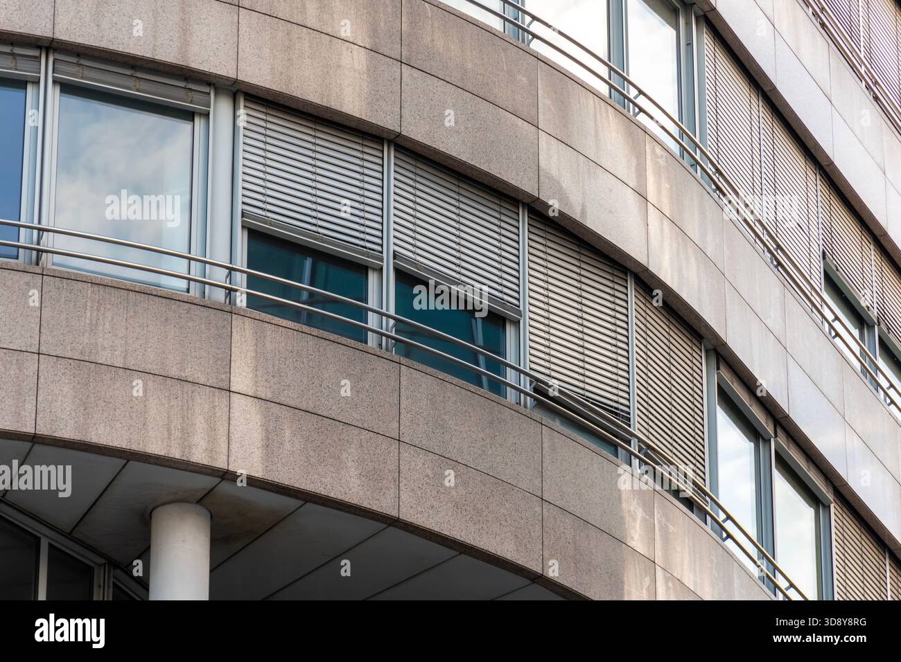 Facciata curva di un moderno edificio per uffici con grandi finestre, persiane esterne e pannelli di rivestimento in pietra. Foto Stock
