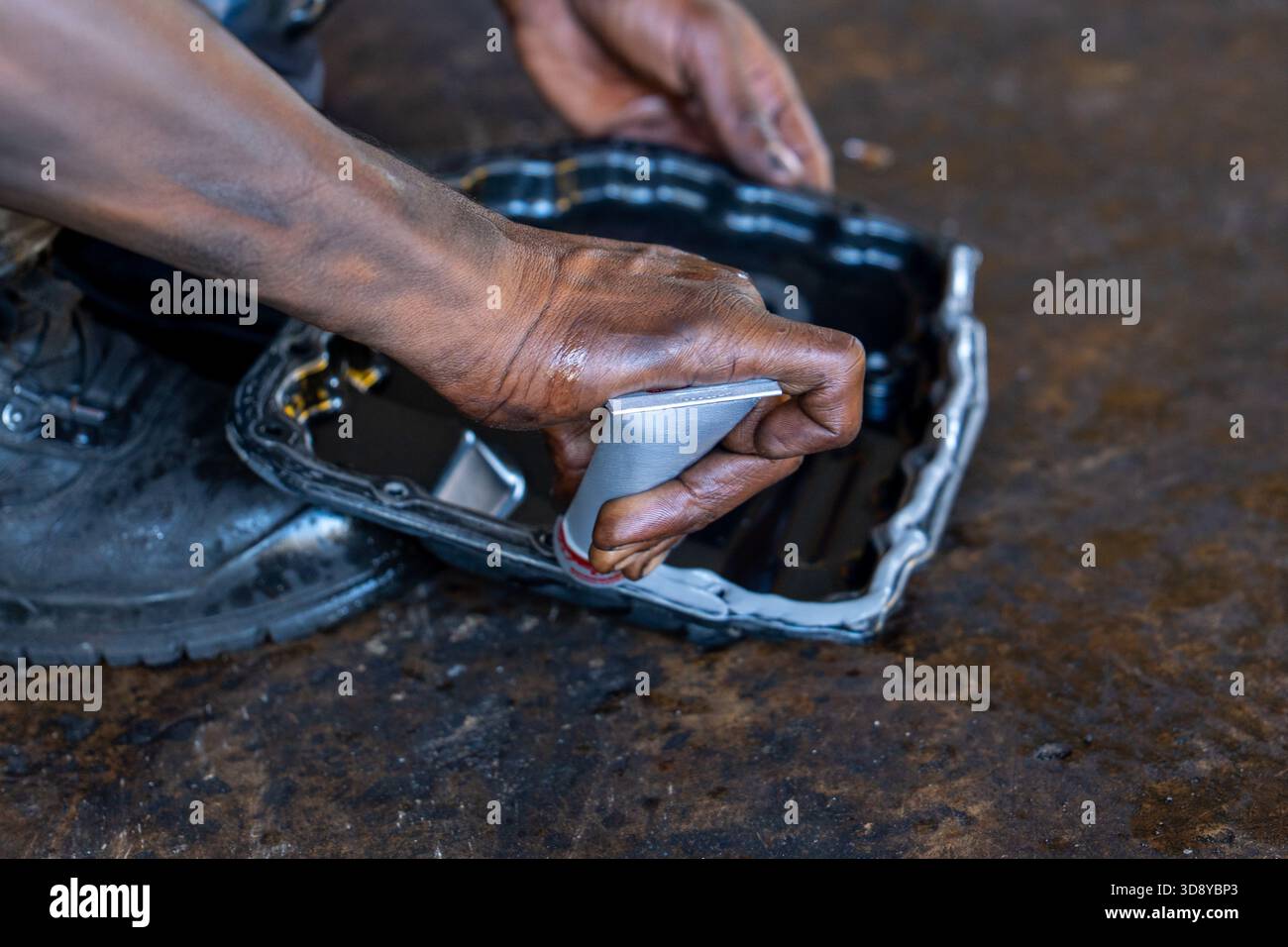 Le mani di un meccanico applicano del sigillante sulla coppa dell'olio della trasmissione di una vettura per un cambio ATF. Servizio automatico, manutenzione del veicolo, riparazione della trasmissione, Foto Stock