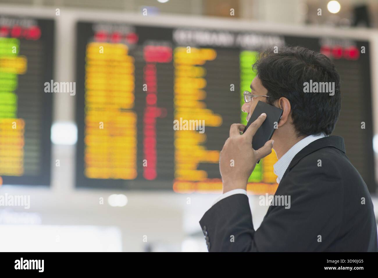 Uomo d'affari asiatico che guarda gli orari dei voli aeroportuali e al telefono Foto Stock