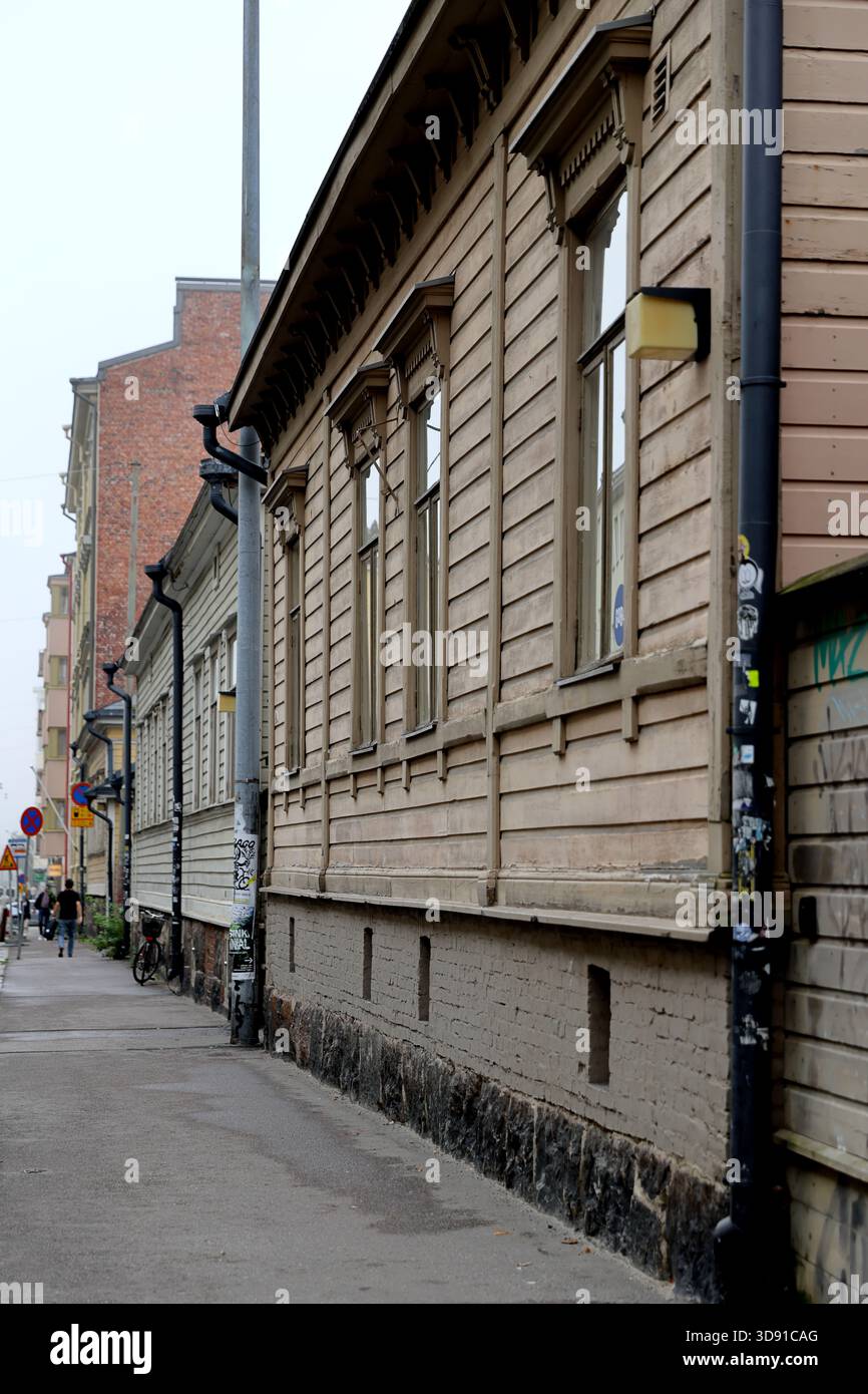 Edifici storici in legno con cornici delle finestre fiancheggiano una strada della città con pedoni e una bicicletta nel centro di Helsinki, in Finlandia, in una giornata d'autunno nuvolosa. Foto Stock