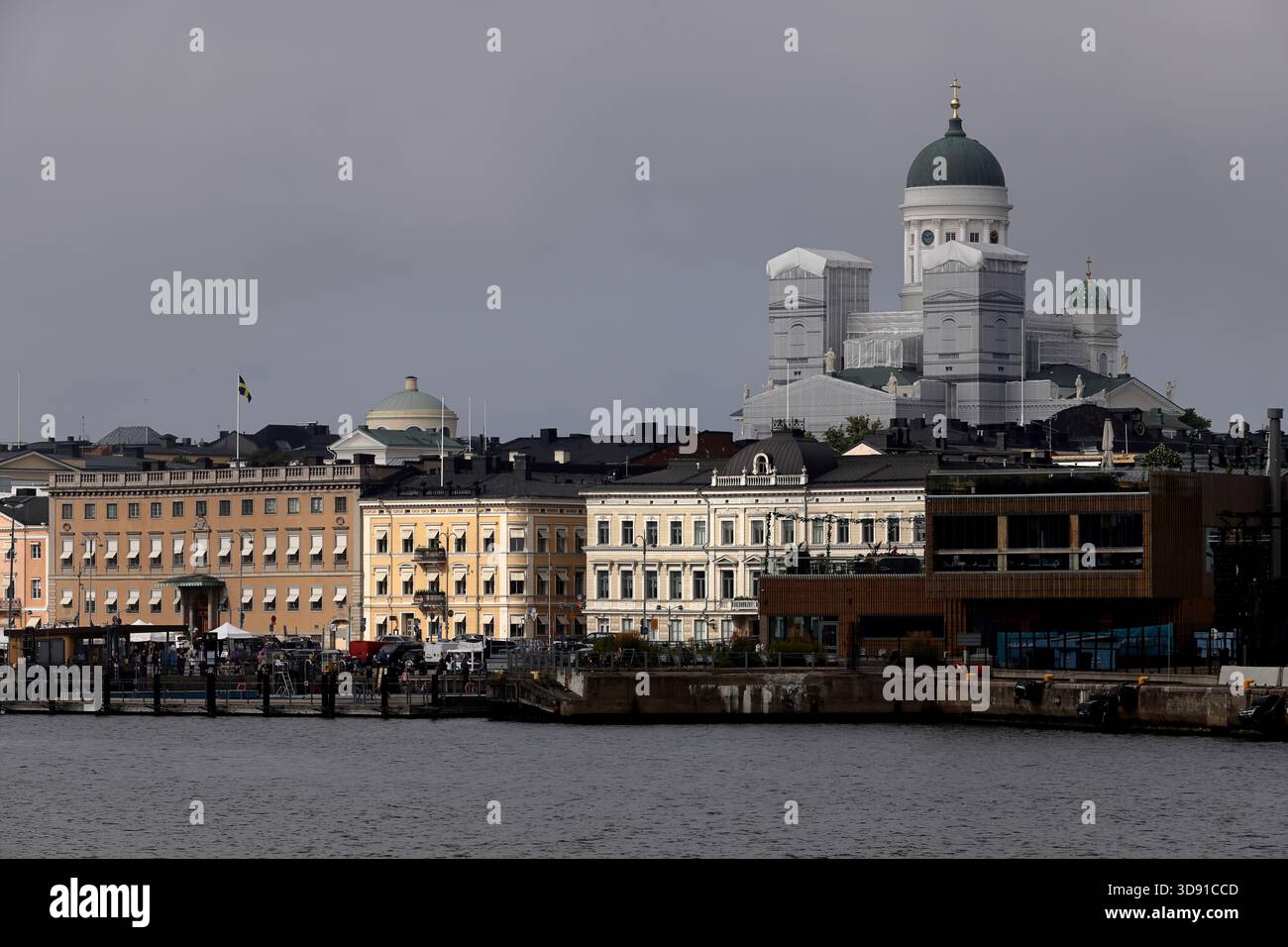 Vista sul lungomare degli edifici storici del porto con la cattedrale di Helsinki e le cupole che si innalzano sopra lo skyline della città di Helsinki, in Finlandia, sotto un cielo nuvoloso. Foto Stock