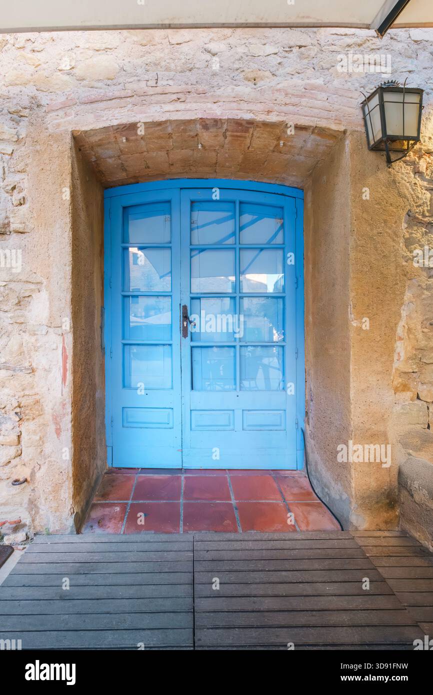 Porta doppia di colore blu vibrante posta in una porta rustica in pietra ad arco e stucco con piastrelle di terracotta e pavimento in legno, lanterna esterna Foto Stock