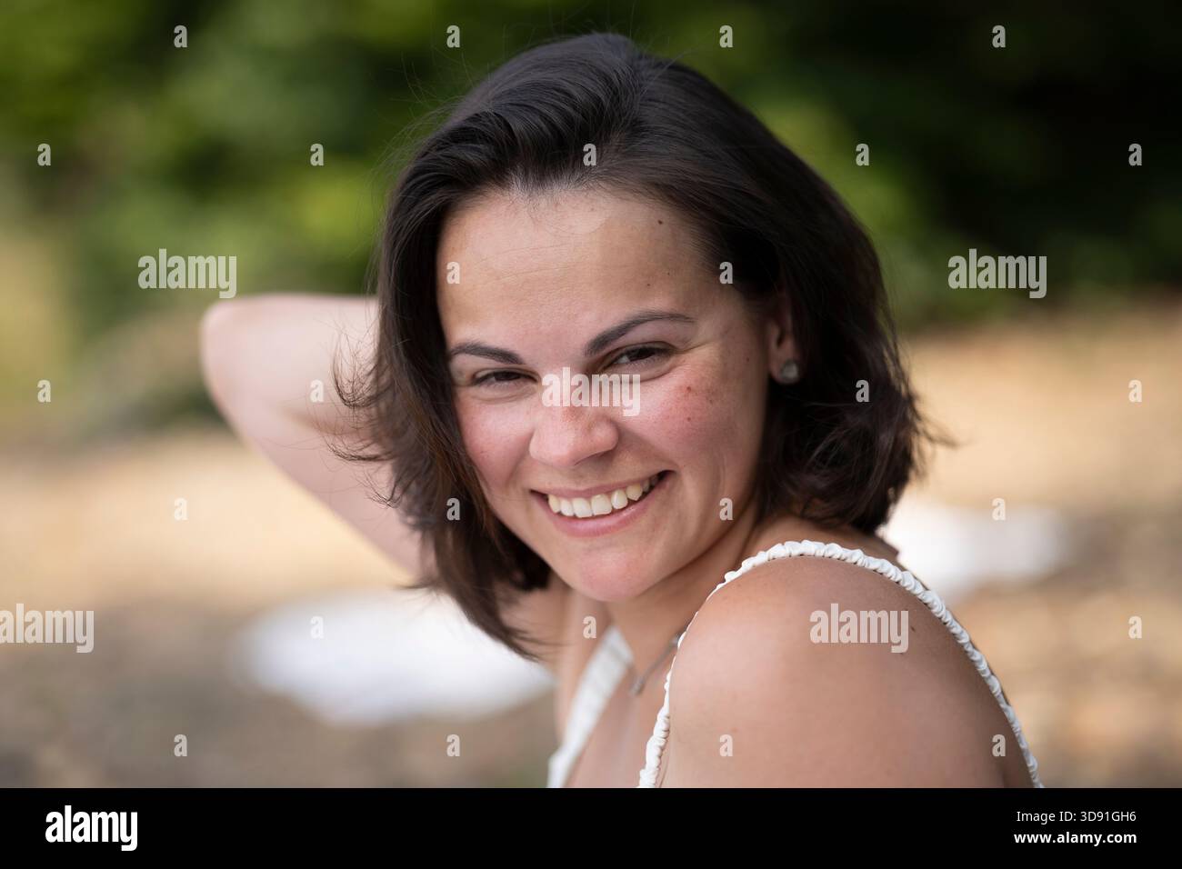 Ritratto orizzontale di una donna bruna sorridente che si tocca i capelli, mostra i denti, concetto di bellezza dentale estiva sulla spiaggia con spazio di copia Foto Stock