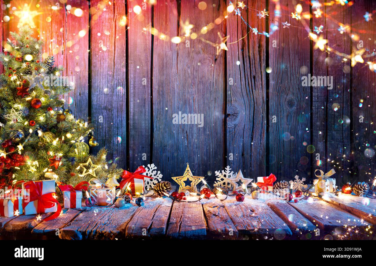 Albero di Natale con scatole regalo su tavolo in legno rustico con ghirlande e decorazioni - Abstract Defocused Lights Foto Stock