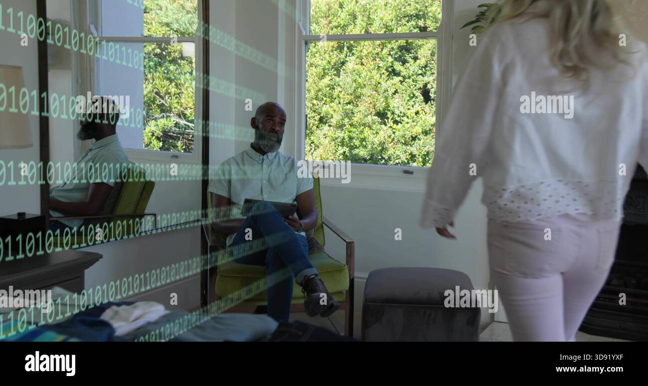 Uomo seduto che tiene un tablet in una sedia verde alla finestra, donna che cammina in pantaloni rosa, sovrapposizione binaria Foto Stock