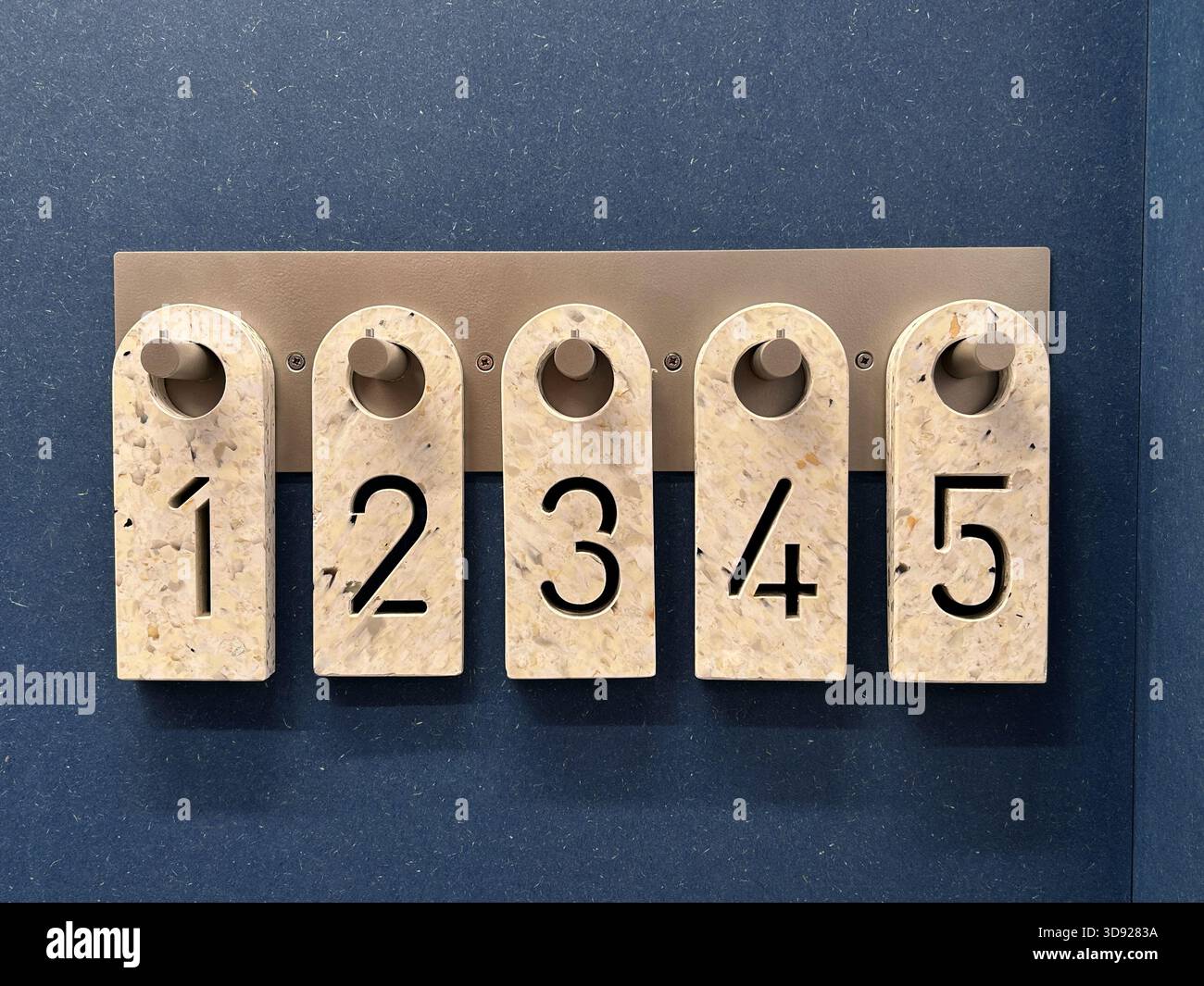 Etichette in plastica numerate appese su un rack metallico all'ingresso di un camerino in un negozio di abbigliamento, utilizzate per organizzare gli articoli dei clienti Foto Stock