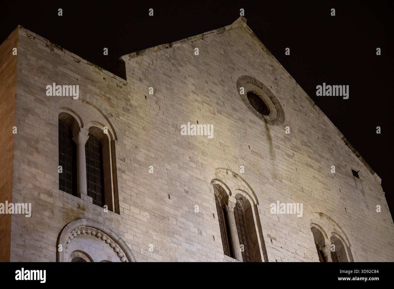 Primo piano sull'imponente facciata in pietra bianca della Basilica di San Nicola a Bari, Italia, caratterizzata da finestre ad arco romaniche e un oculo sotto Foto Stock