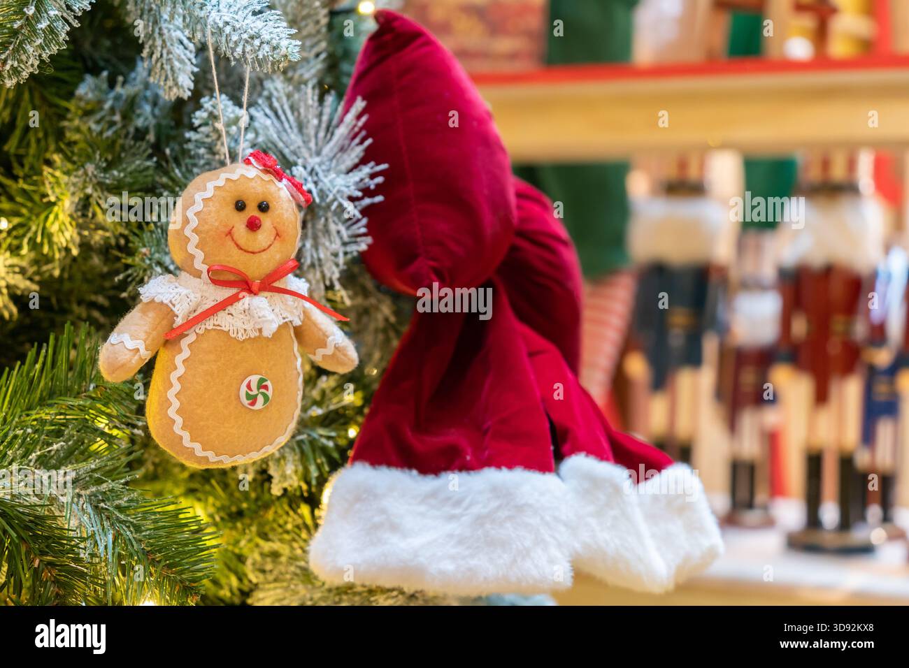 Un allegro ornamento di pan di zenzero con finitura a glassa e un fiocco rosso pende tra i rami dell'albero di Natale spolverati di neve, illuminati da luci calde. Foto Stock