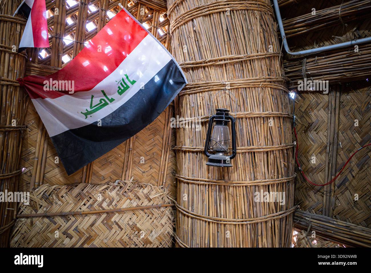 Nasiriyah, Iraq - 20 novembre 2025: Primo piano della bandiera irachena e una Lanterna al cherosene su una colonna di reed in un Mudhif Foto Stock