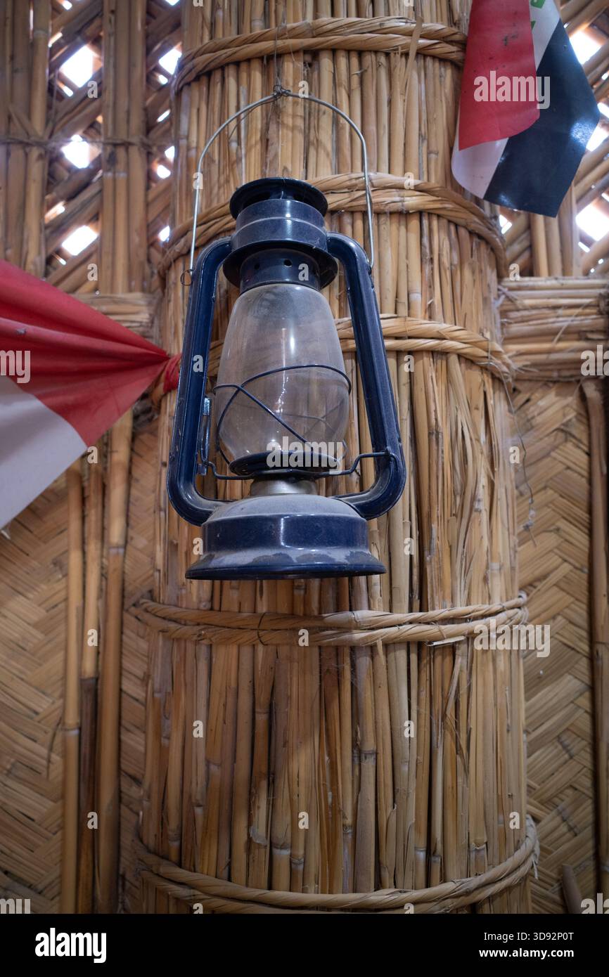 Nasiriyah, Iraq - 20 novembre 2025: Primo piano della bandiera irachena e una Lanterna al cherosene su una colonna di reed in un Mudhif Foto Stock