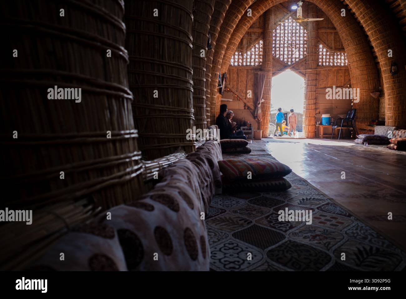Nasiriyah, Iraq - 20 novembre 2025: Persone che socializzano all'interno di un tradizionale Mudhif di canna con la luce del sole che scorre attraverso l'ingresso Foto Stock