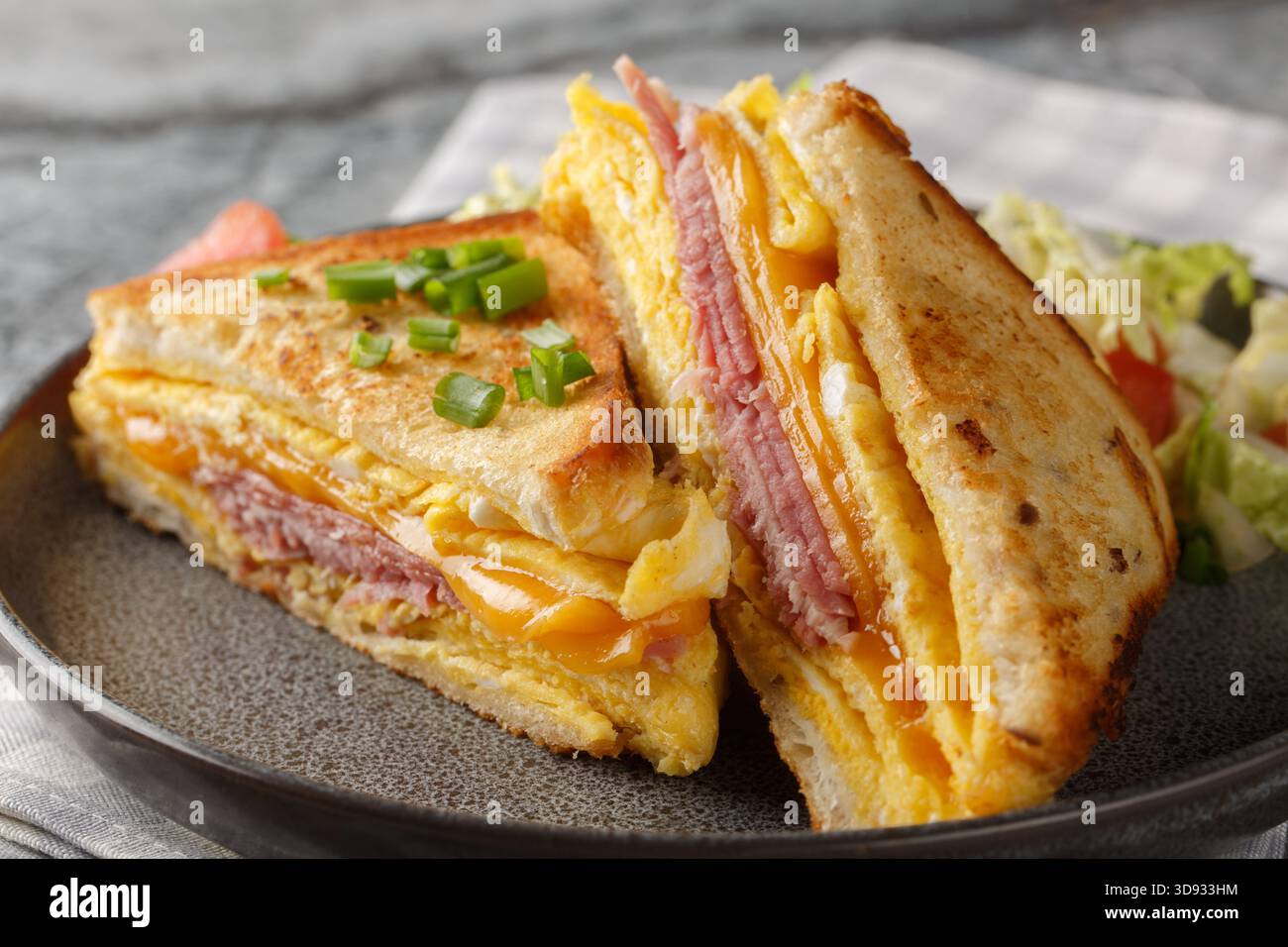 Sandwich caldo con omelette all'uovo, formaggio e prosciutto da vicino in un piatto sul tavolo. Orizzontale Foto Stock