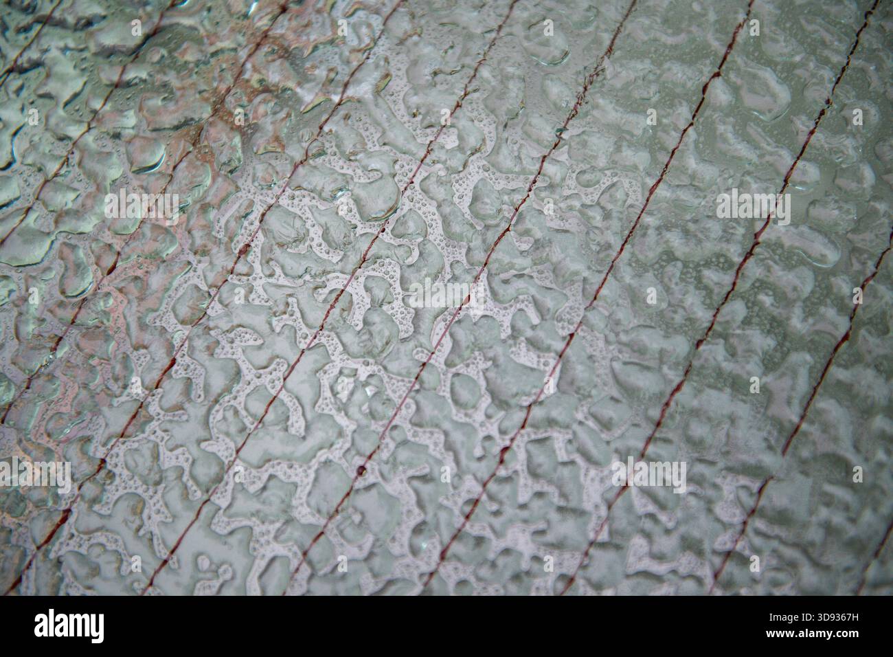 Superficie bagnata del finestrino posteriore di un'auto con una serie di linee e goccioline d'acqua. Le goccioline di ghiaccio sono sparse sulla superficie, creando un senso di Foto Stock