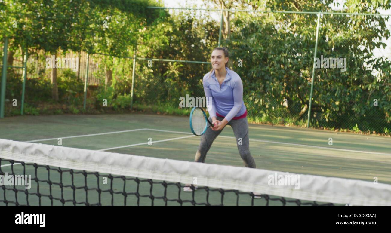 Con una racchetta da tennis, una donna che si prepara al campo duro con la rete e indossa la maglia viola Foto Stock
