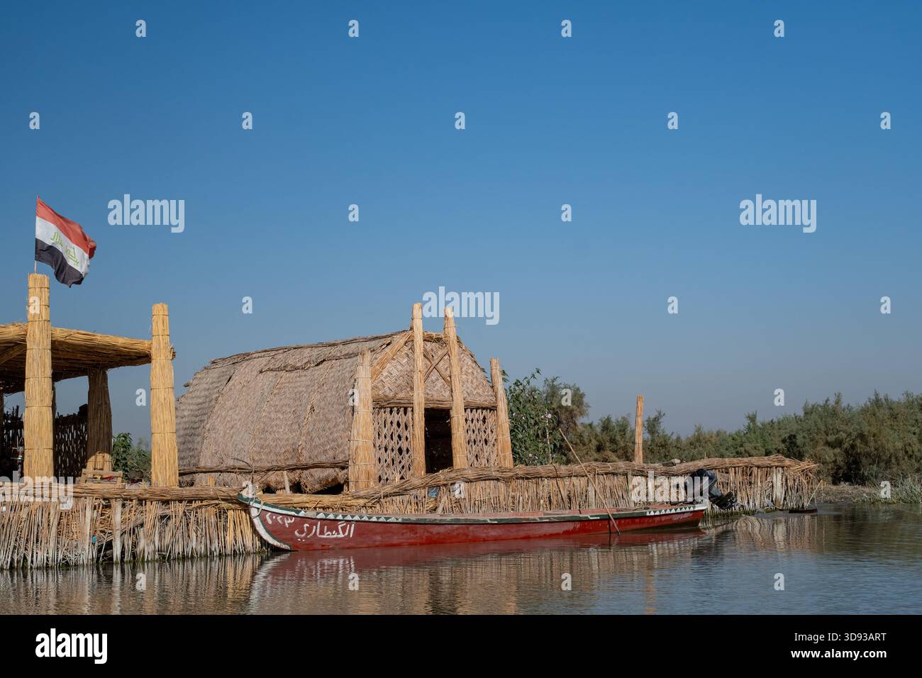 Nasiriyah, Iraq - 20 novembre 2025: Tradizionale Reed Mudhif e Mashoof ormeggiato battello che vola la bandiera irachena nelle paludi Chibayish Foto Stock
