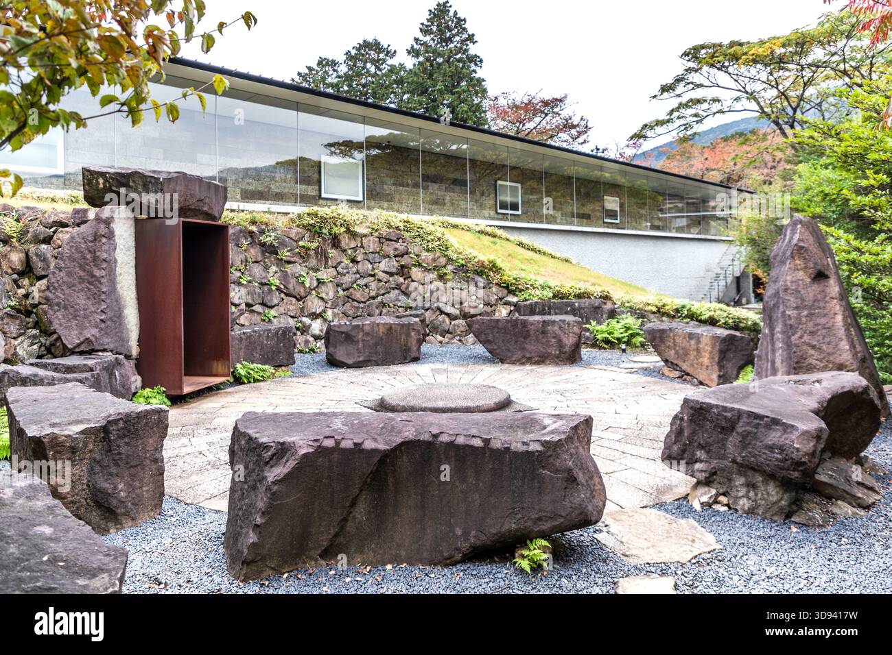 Un cerchio di pietre con una vecchia pietra milleriva nel cortile dell'Osservatorio Enoura (江之浦測候所) a Odawara, prefettura di Kanagawa, Giappone. La disposizione dei blocchi di basalto che circondano una mola centrale su una superficie di ghiaia ricorda le strutture circolari preistoriche; sullo sfondo si trovano il vetro della galleria e un telaio in acciaio Corten. Hiroshi Sugimoto incorporò nell'installazione manufatti di varie epoche Foto Stock