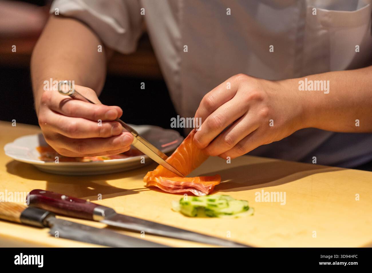 Lo chef esperto sta affettando salmone fresco con un coltello affilato in una cucina moderna, mostrando competenza culinaria e attenzione ai dettagli. Foto Stock