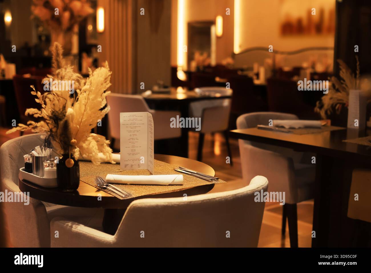 Elegante ambiente da tavola del ristorante con menu', posate e fiori secchi in vaso sotto una calda illuminazione ambientale. Foto di alta qualità Foto Stock