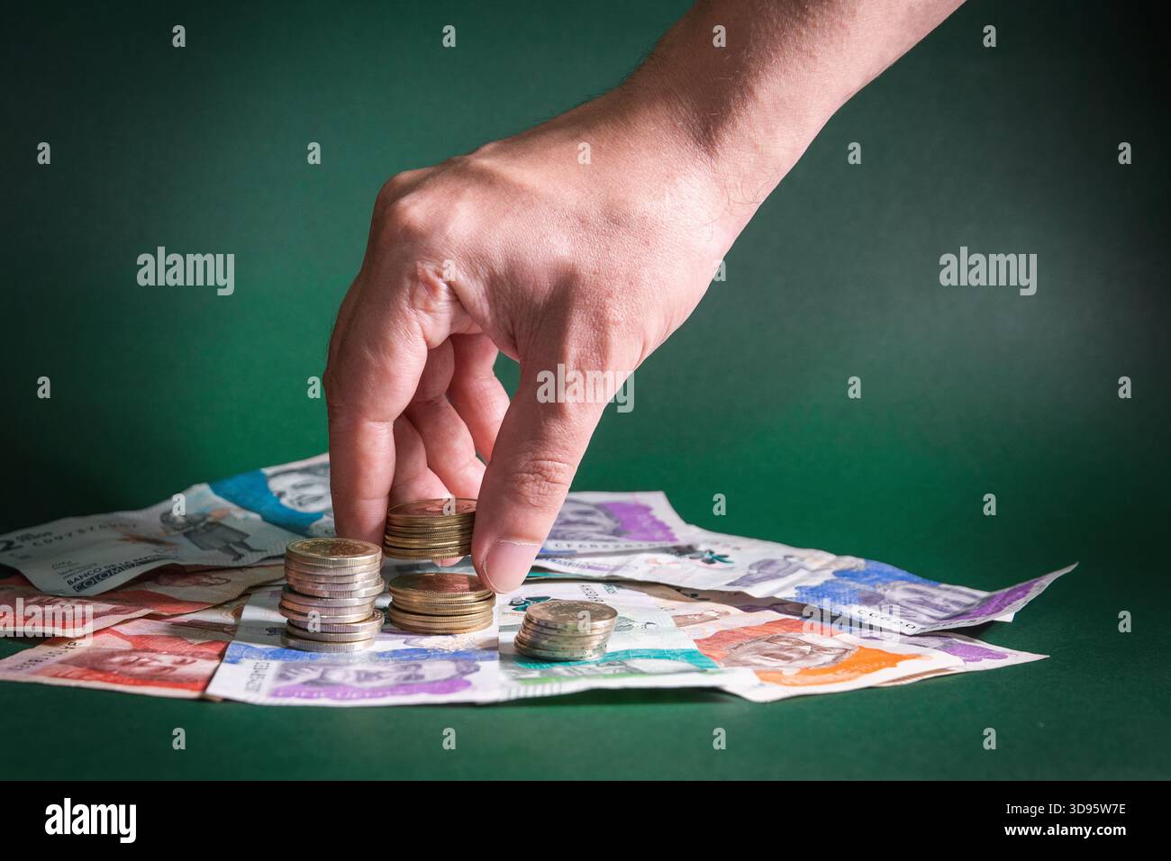 Accatastare a mano monete sopra le banconote in peso colombiano, simboleggiando la crescita dei risparmi, la pianificazione finanziaria, le decisioni di investimento economico e il creat Foto Stock