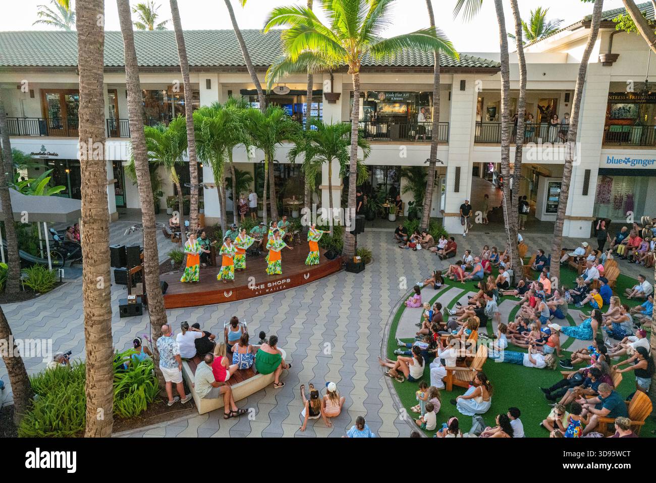 Una folla guarda i tradizionali artisti hawaiani ballare al centro commerciale all'aperto Shops. Foto Stock