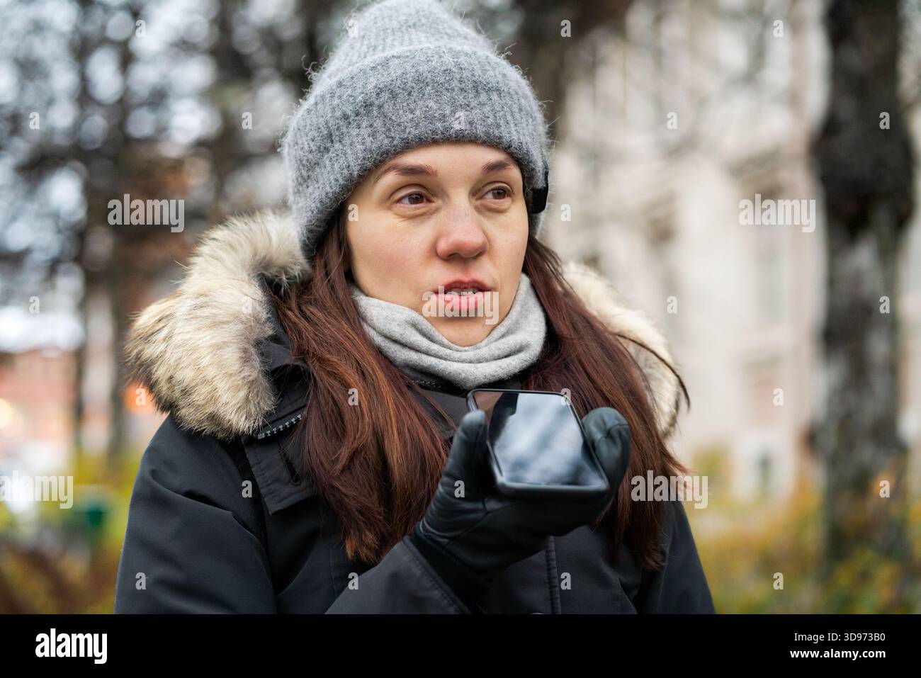 Messaggio vocale. Donna che parla con il vivavoce in inverno. Invia audio mobile in città. Tenere lo smartphone vicino alla bocca. Registrare la nota audio. Foto Stock