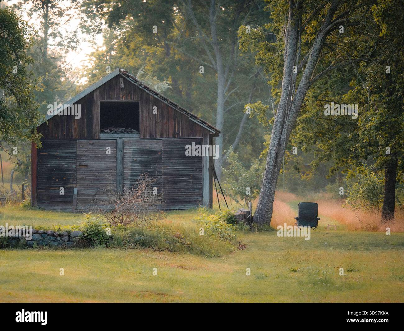 Vecchio fienile svedese in legno nel tranquillo paesaggio rurale del villaggio con sedia vuota Foto Stock
