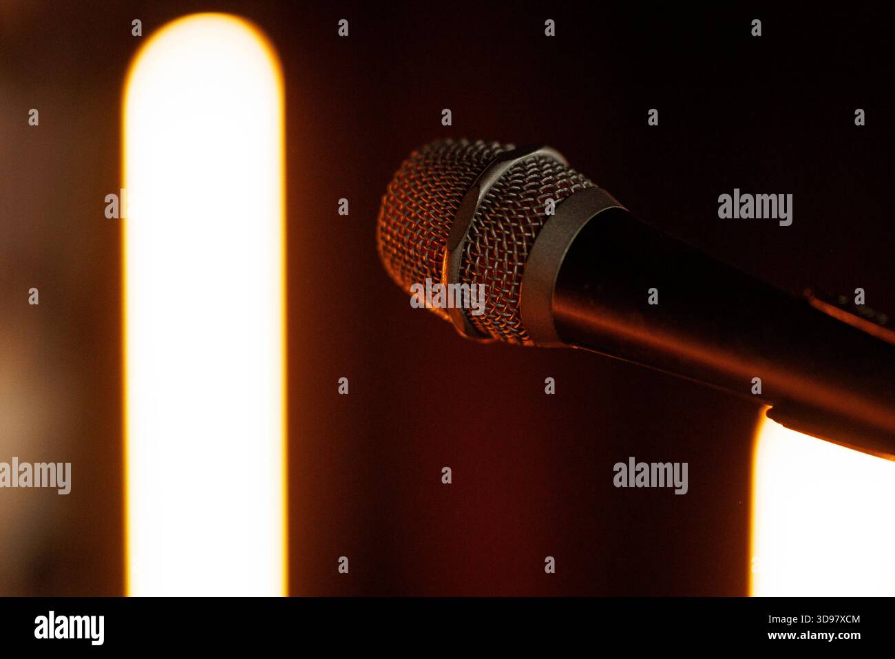 Primo piano di un microfono dinamico illuminato da luci ambiente calde. Composizione minimale che enfatizza le prestazioni musicali e la registrazione audio. Foto Stock