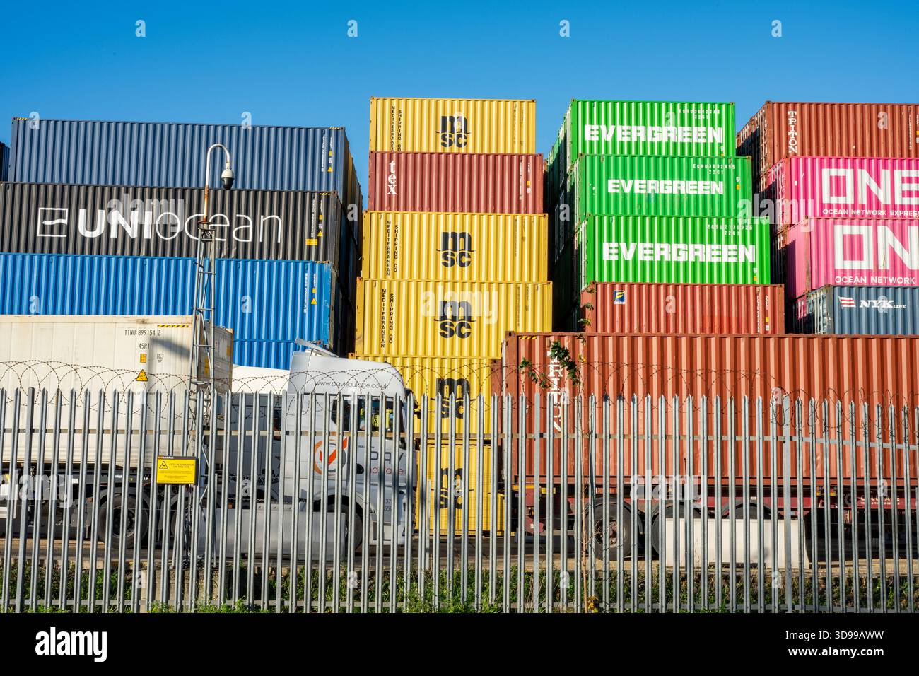 Contenitori per spedizioni colorati impilati in un luogo sicuro con filo di rasoio e recinzioni a palizzata nel porto di Southampton Docks, Regno Unito Foto Stock