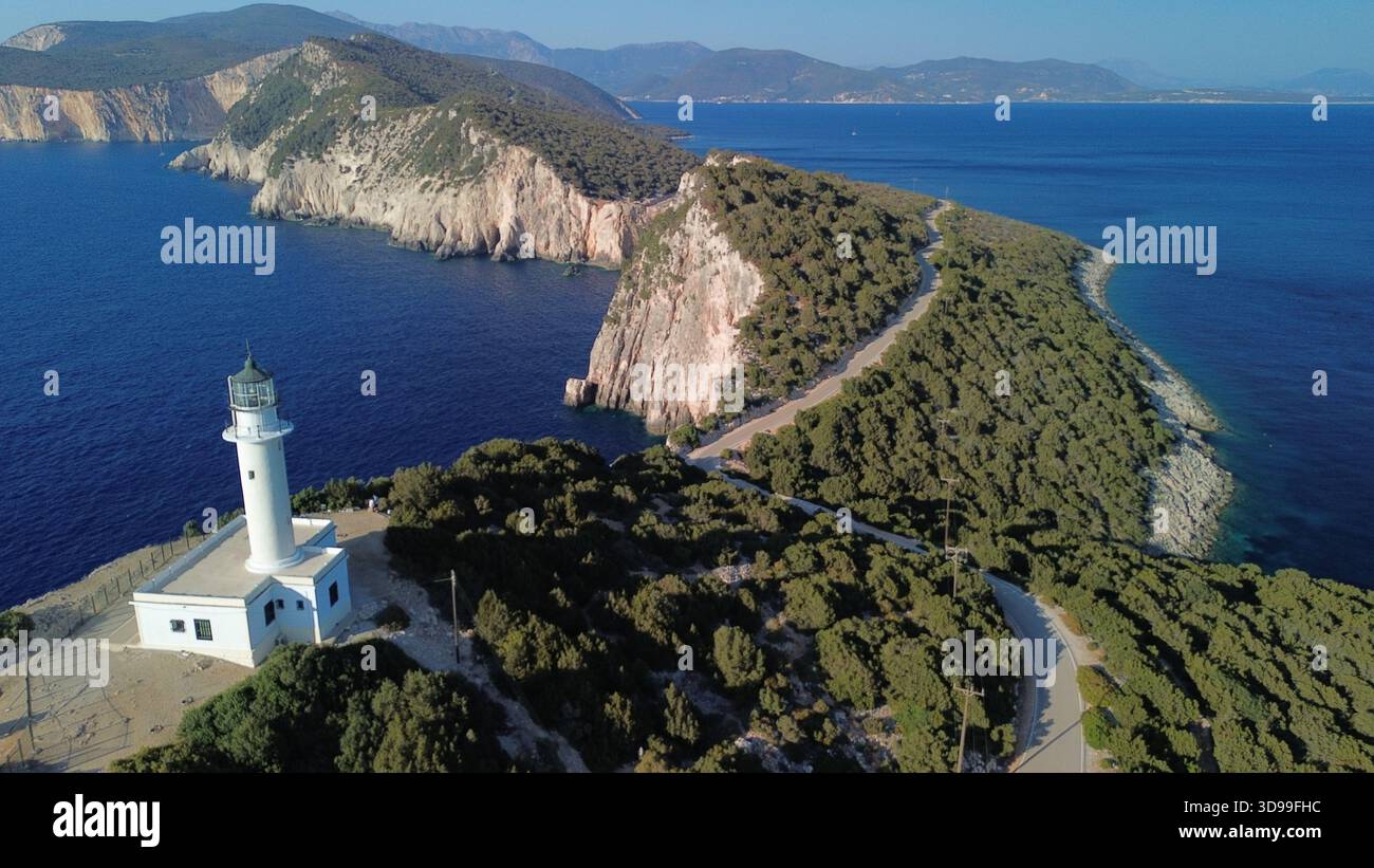 Faro bianco su una collina boscosa sopra il mare blu profondo, con strada tortuosa e aspre scogliere costiere. Foto Stock