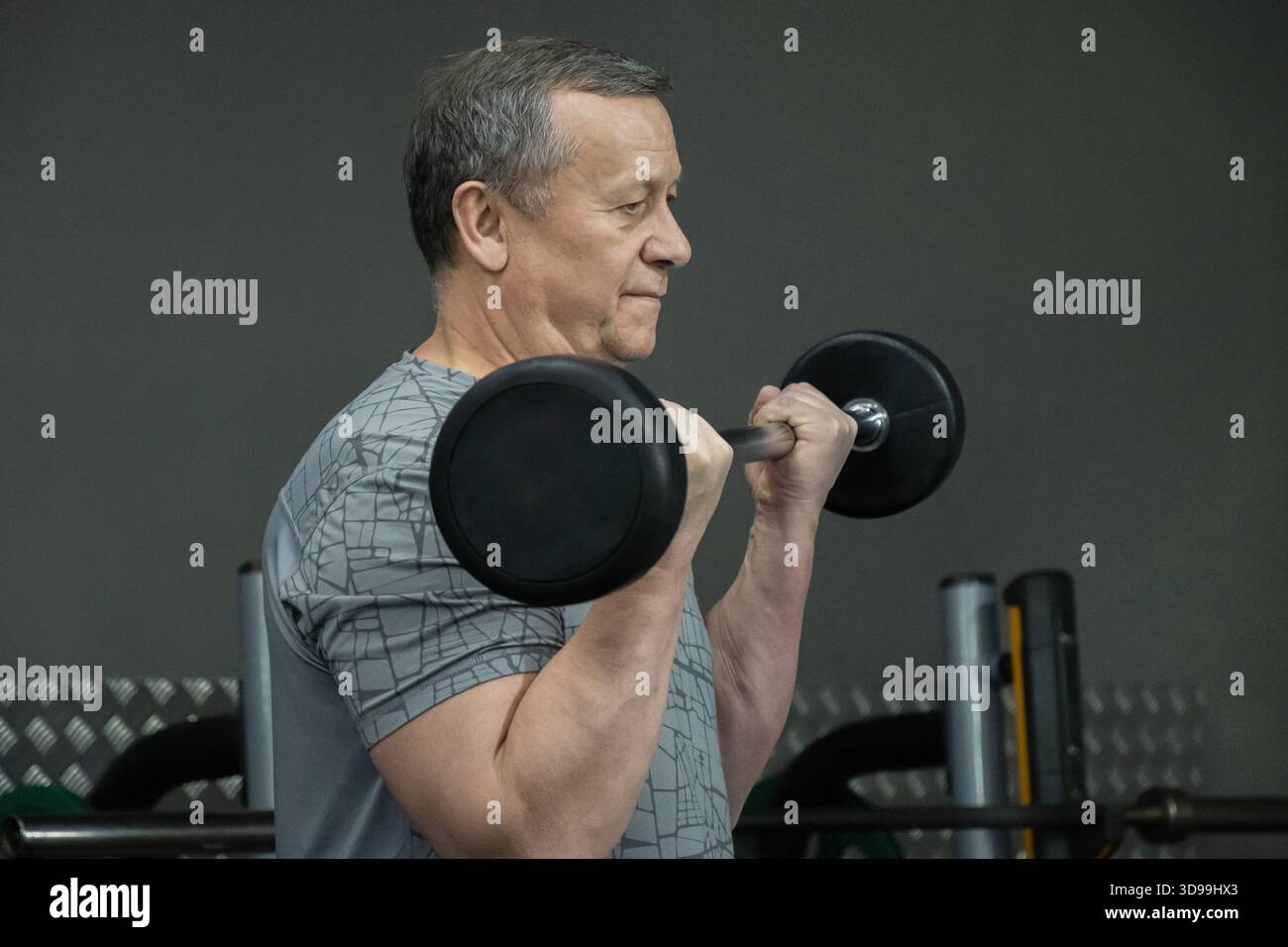 Uomo adulto allenamento con un barbell in palestra, esercizio di forza per una sana forma fisica e lo sviluppo muscolare. Allenamento concentrato. Foto Stock